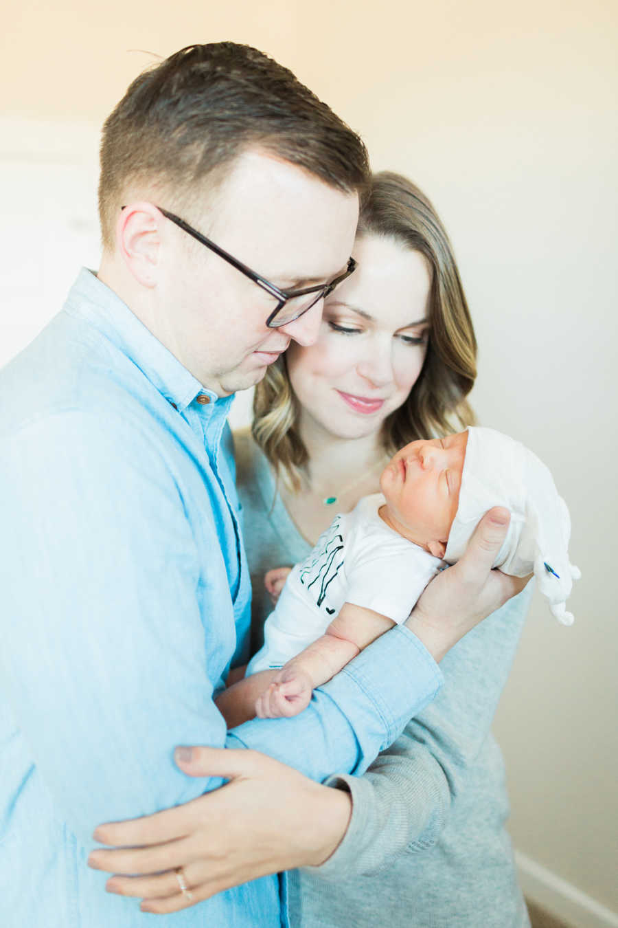 Father stands holding adopted newborn while wife hugs him