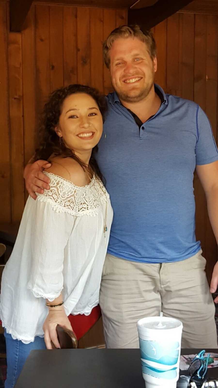 Husband and wife stand smiling beside restaurant table