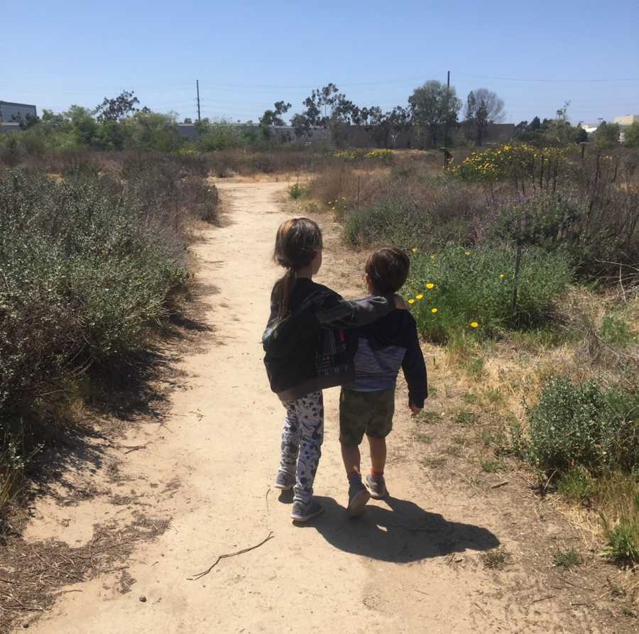 Brother and sister walk on dirt path before they are diagnosed with brain cancer