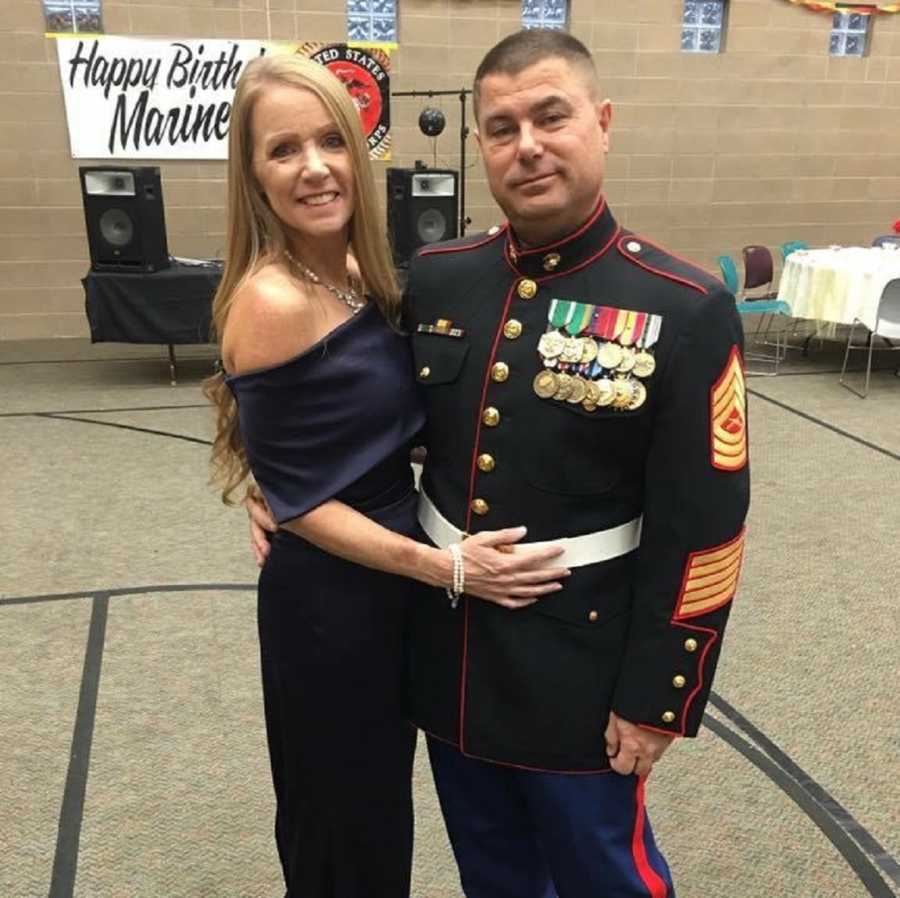 Woman in formal gown stands smiling beside marine husband