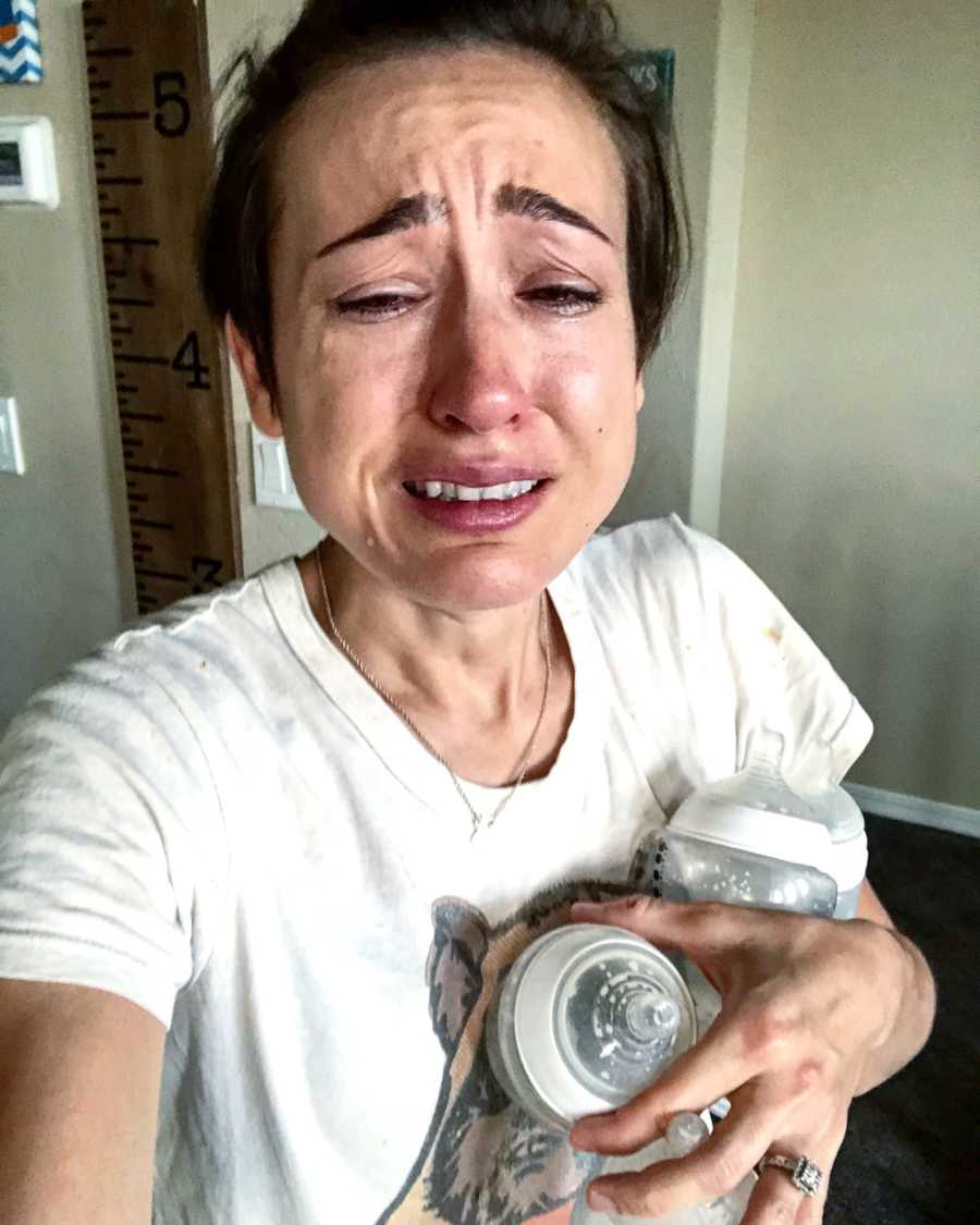 Mother cries in selfie in home as she holds two empty baby bottles