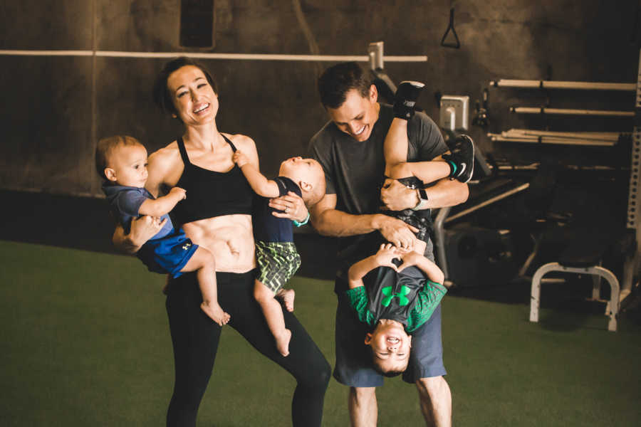 Husband and wife hold their three kids as they stand in gym