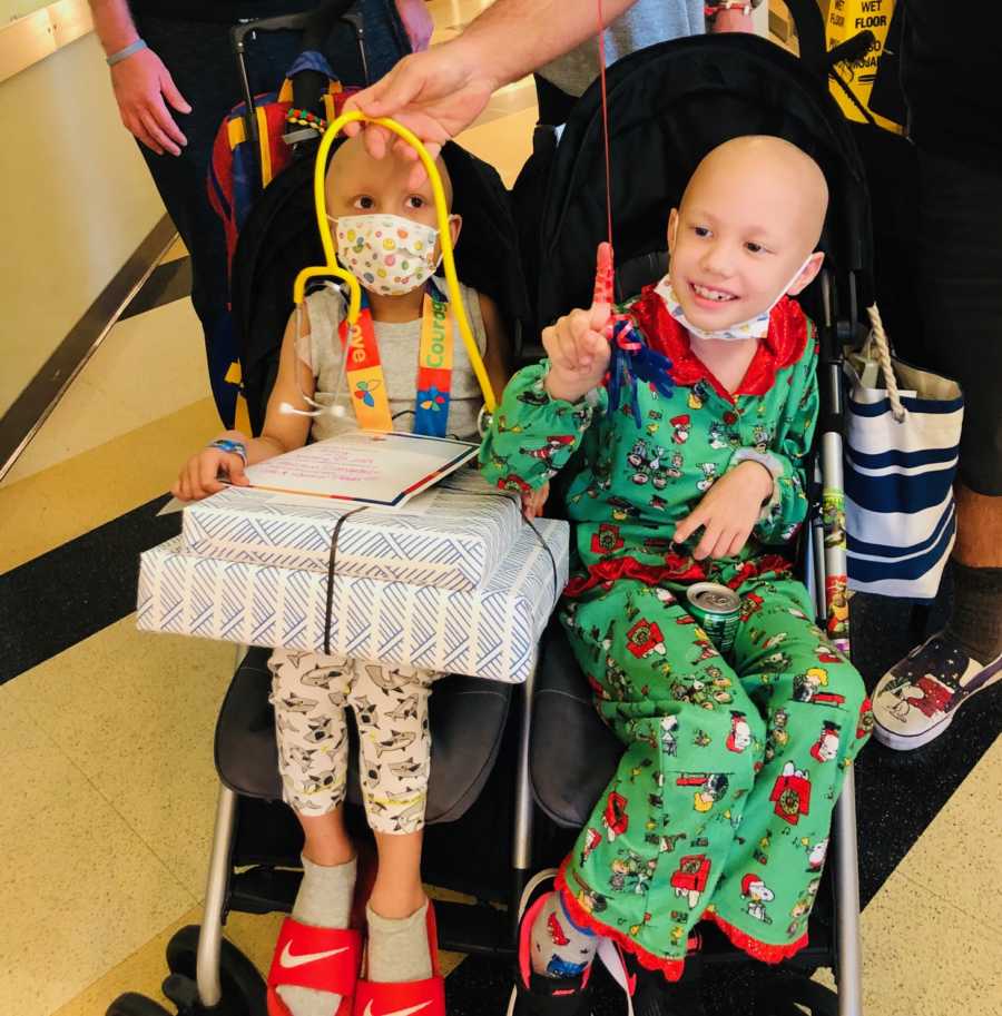 Little boy who beat cancer sits in stroller with presents in his lap beside sister in stroller who is battling cancer