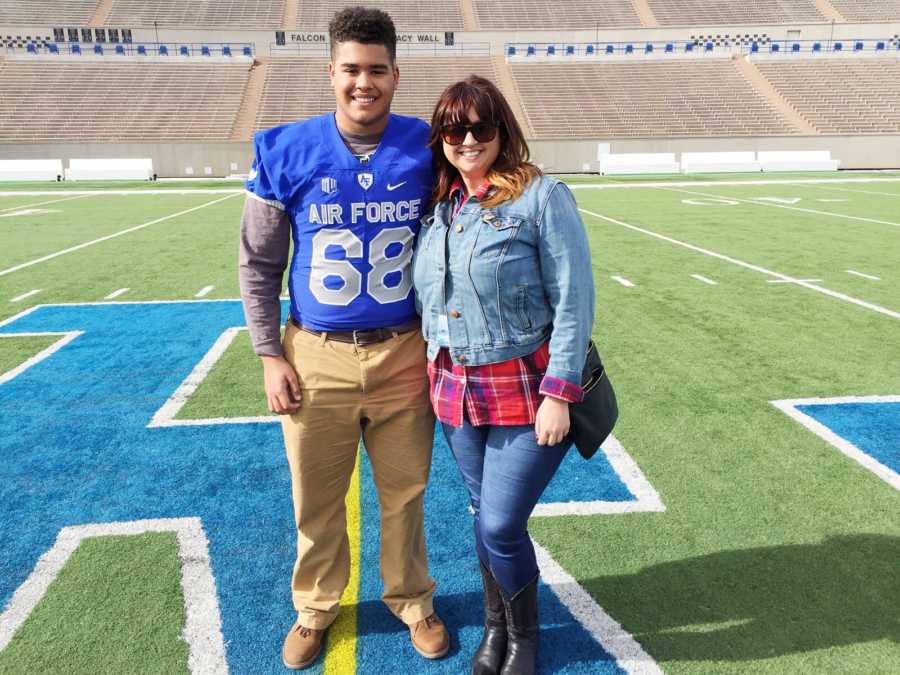 Mother stands on Air Force football field with son wearing Air Force jersey