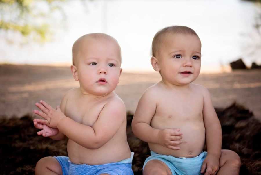 Twin boys sit outside in blue shorts