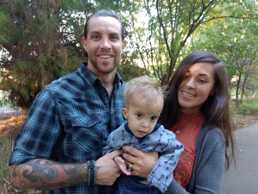 Mother and father stand outside smiling while they hold baby son with unknown disease
