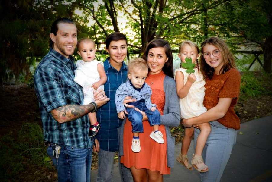 Mother stands outside holding baby with unknown disease beside husband and four other kids