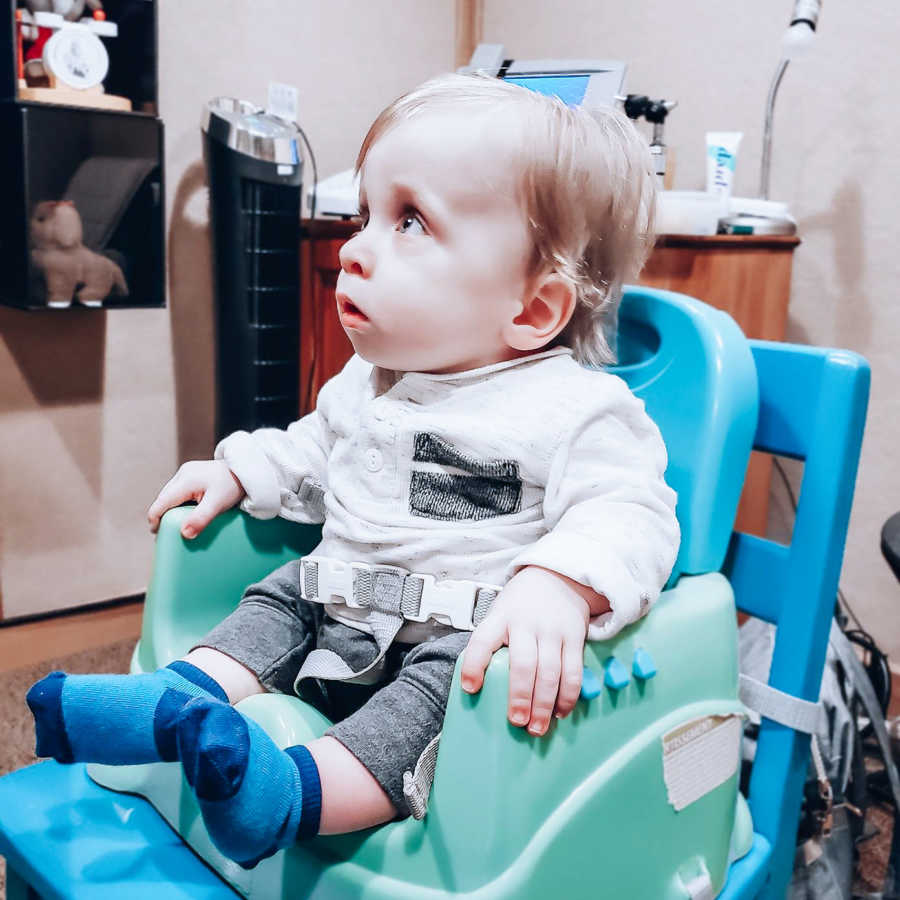 Baby boy with dwarfism sits in high chair in doctor's office