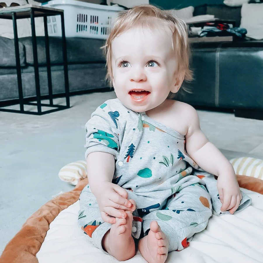 Baby boy sits smiling on pillow on floor