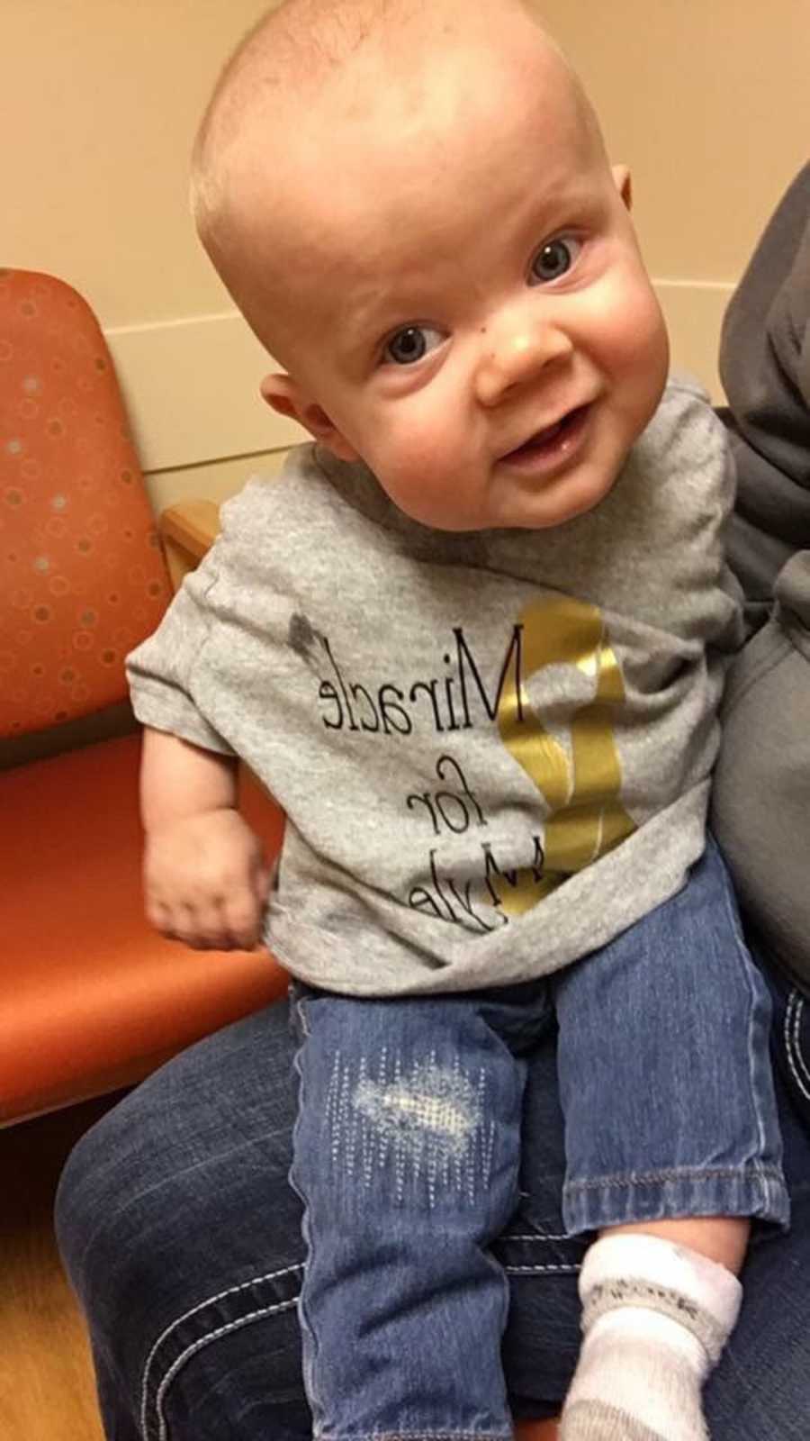 Little boy who has stable tumor smiles while sitting on parent's lap in doctor's office