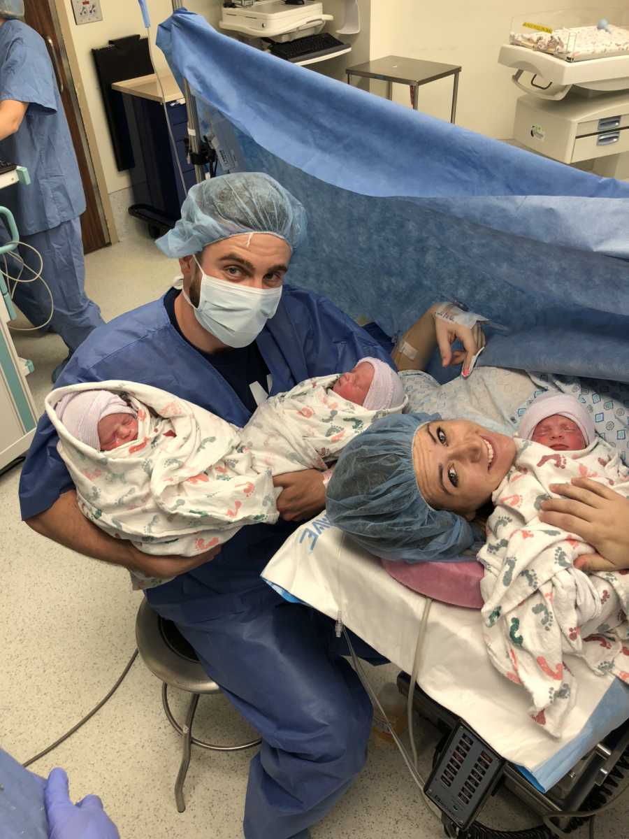 Mother who has c-section lays in operating room holding one triplet while husband holds other two