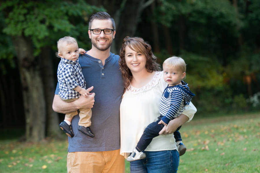 Husband and wife stand outside holding their two foster sons