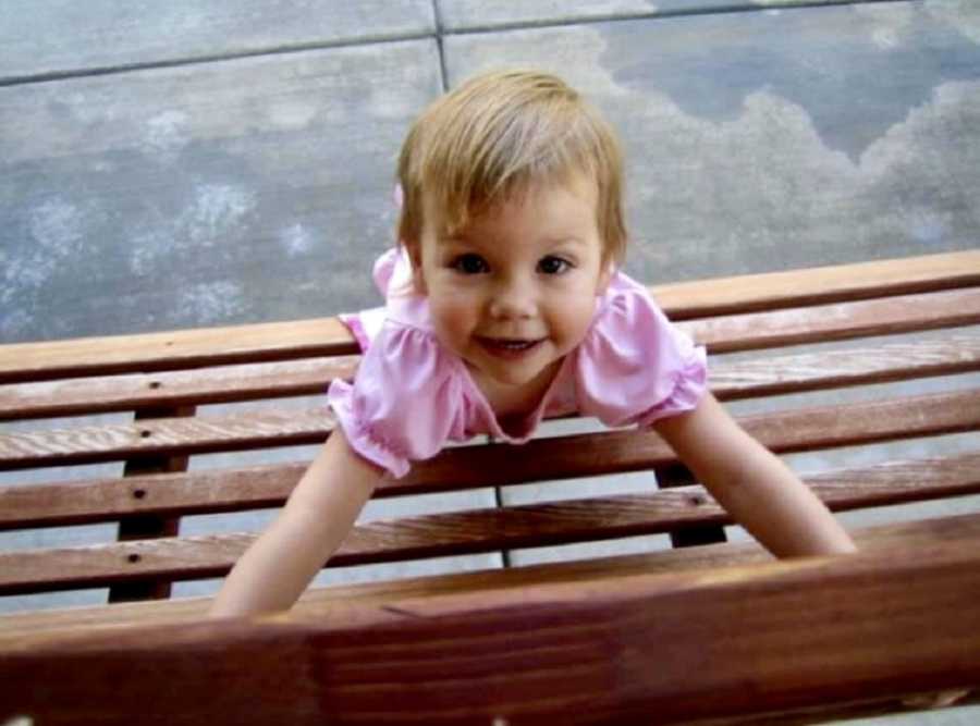Little girl stands beside wooden bench