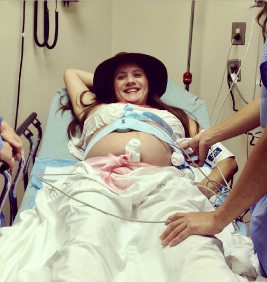Woman pregnant with triplets lays in hospital bed with birthing band on as nurse tends to her