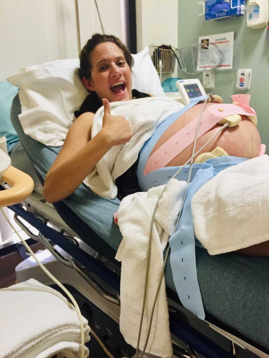 Woman pregnant with triplets lays in hospital bed with thumbs up