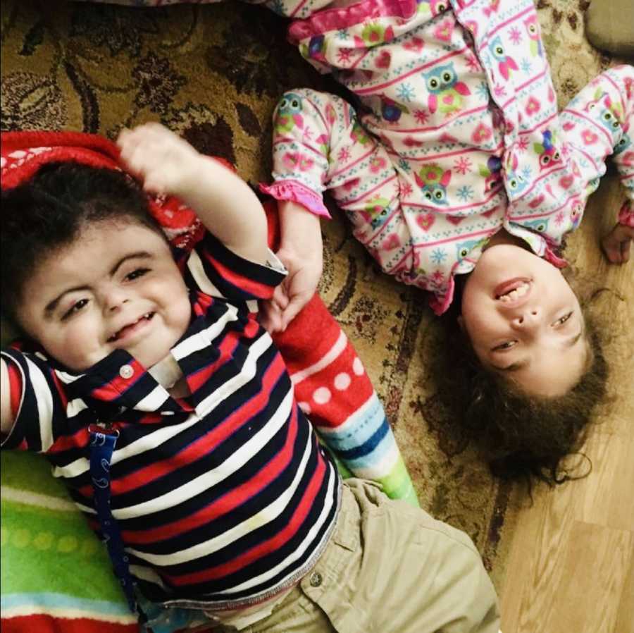 Baby boy with Cornelia de Lange Syndrome lays on floor beside foster sister who has special needs