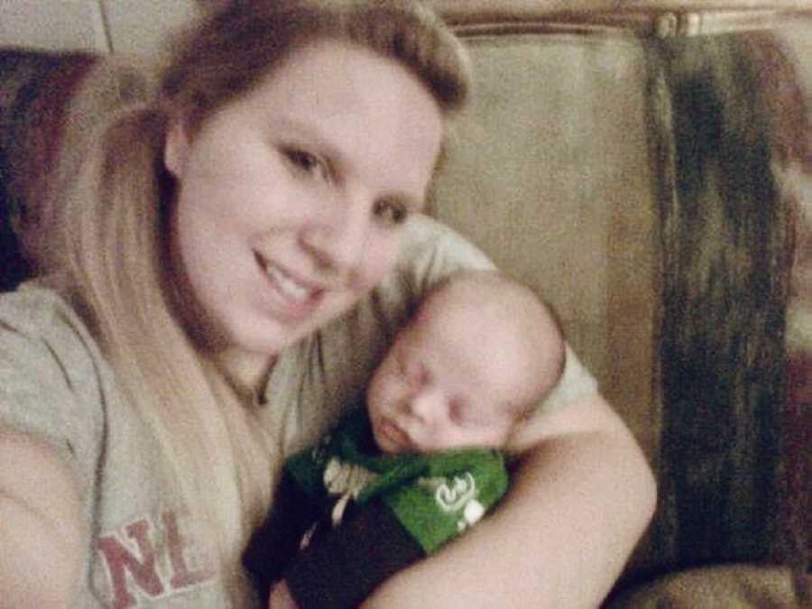 Mother who has miscarried several times sits on couch holding newborn in selfie