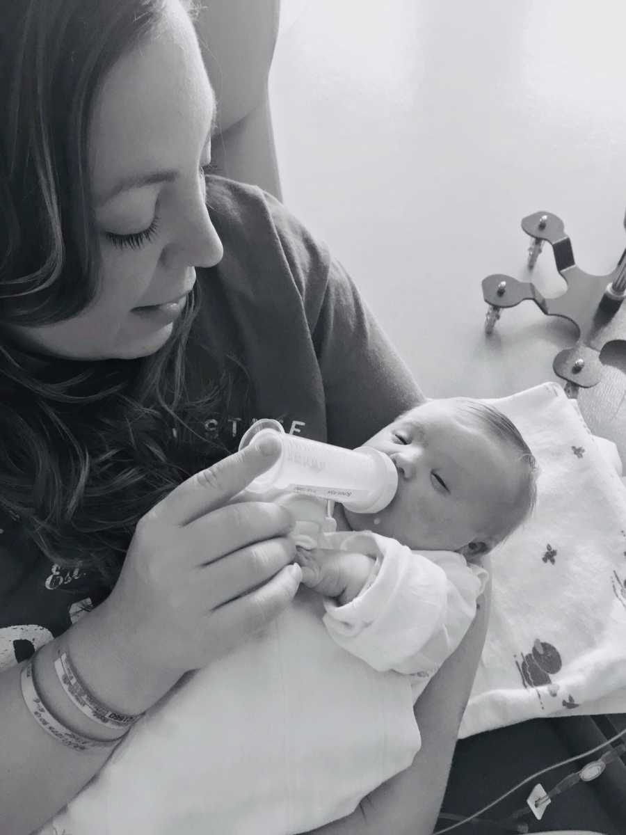 Mother sits in chair feeding newborn with bottle 