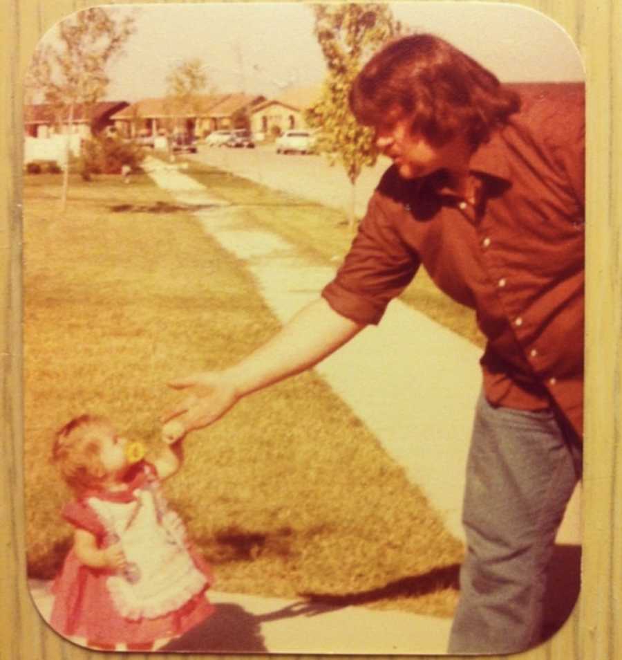 Father stands in driveway holding baby daughter's hand