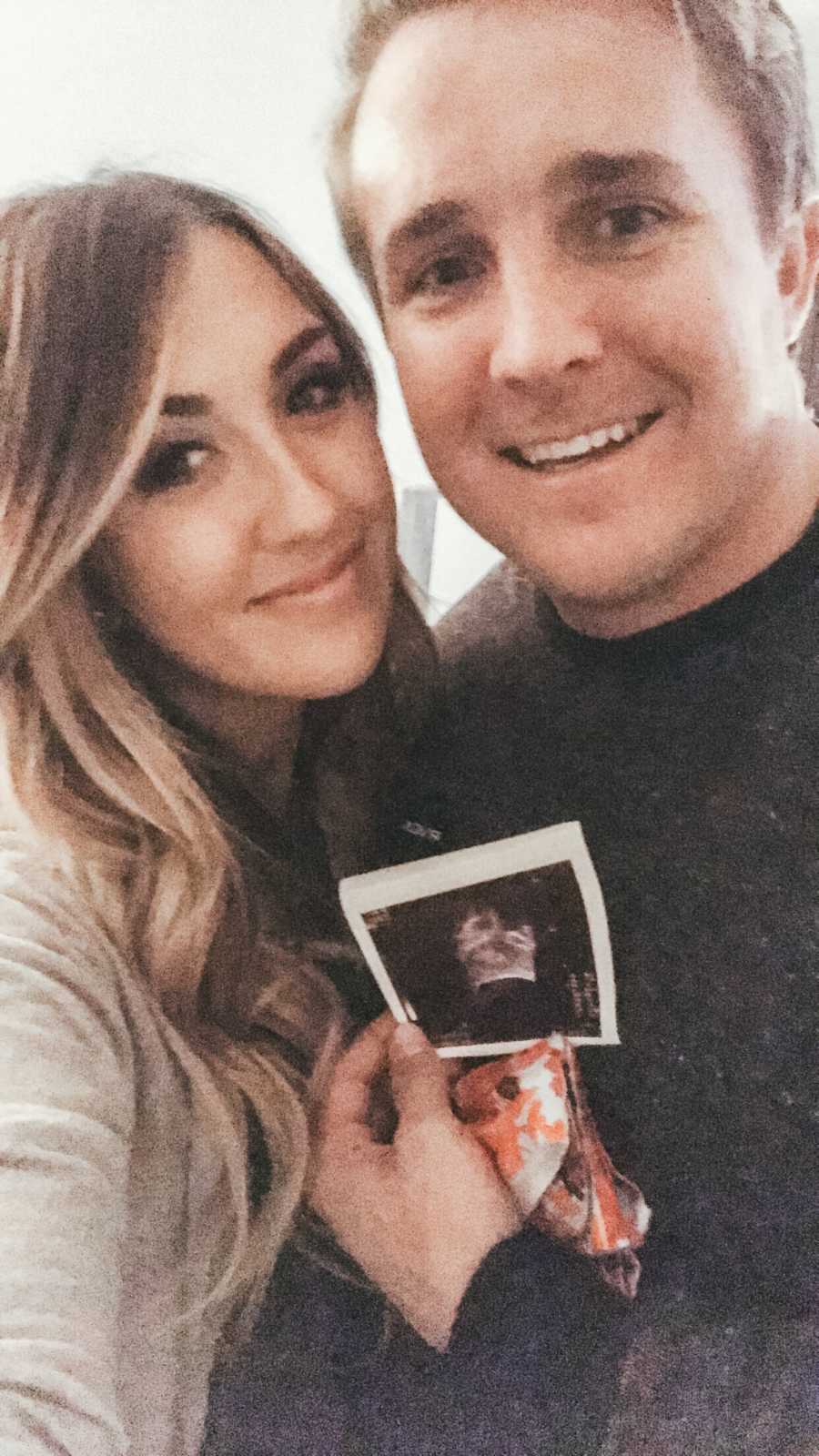 Husband smiles in selfie holding ultrasound picture beside wife who ended up miscarrying