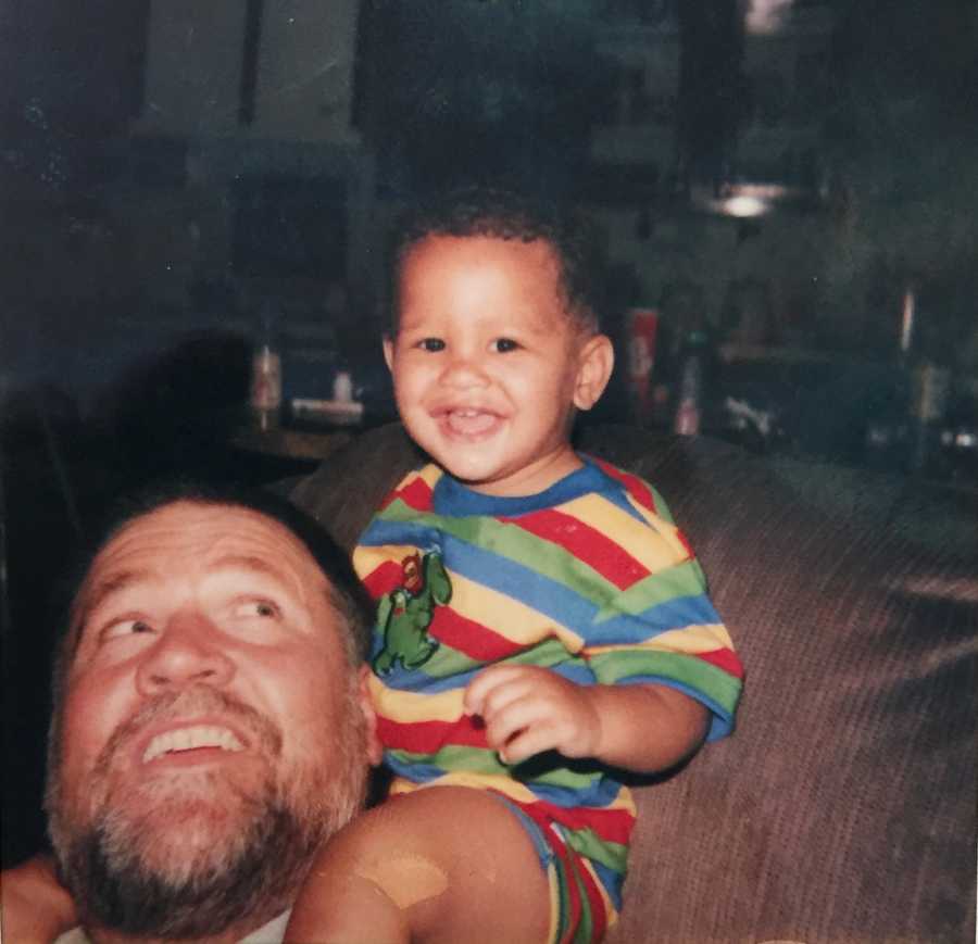 Grandfather sits looking over his shoulder at baby boy sitting on his shoulders