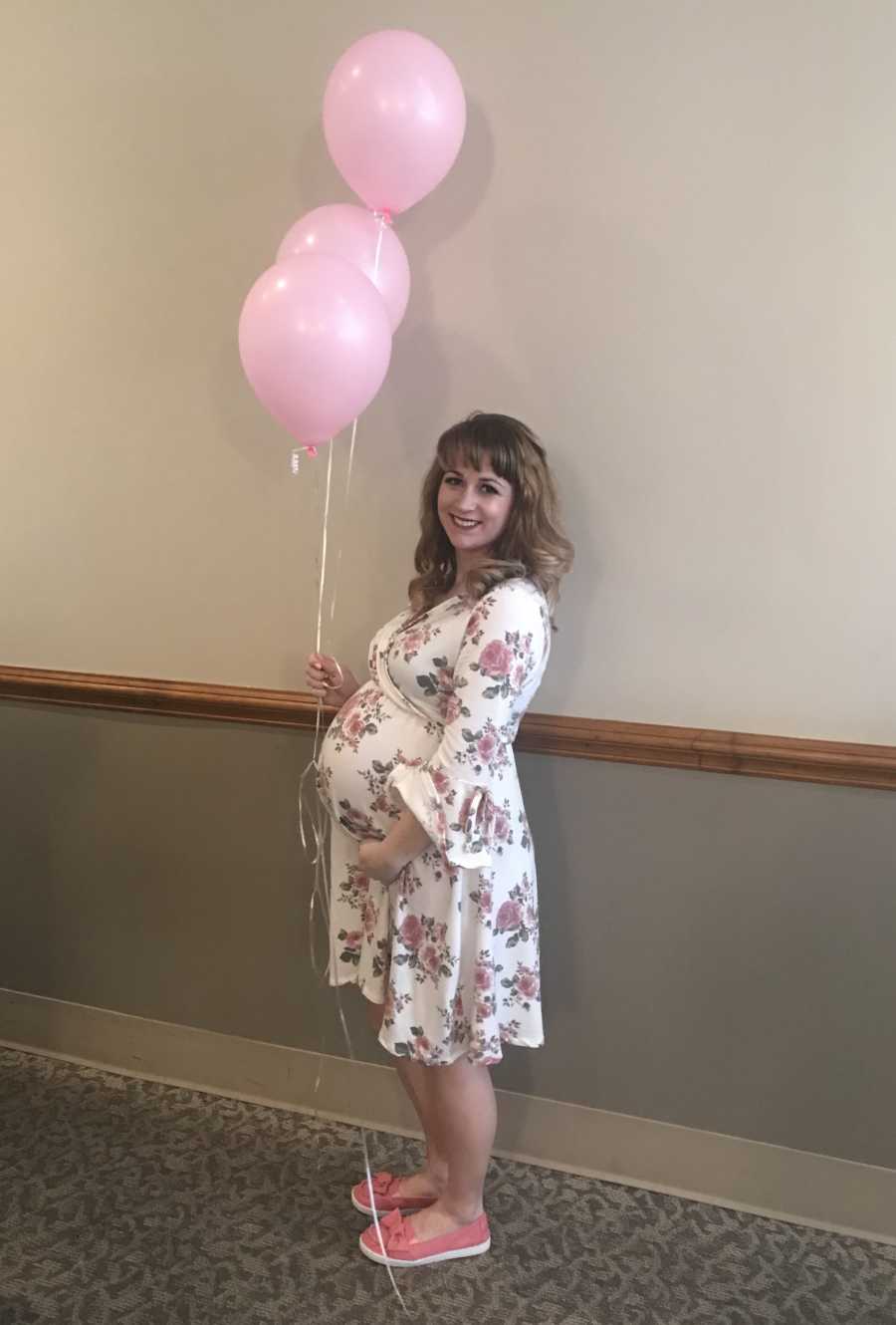 Pregnant woman stands in doctor's office holding pink balloons