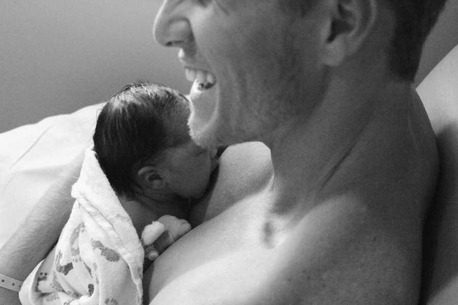 Man smiles as newborn lays on his bare chest