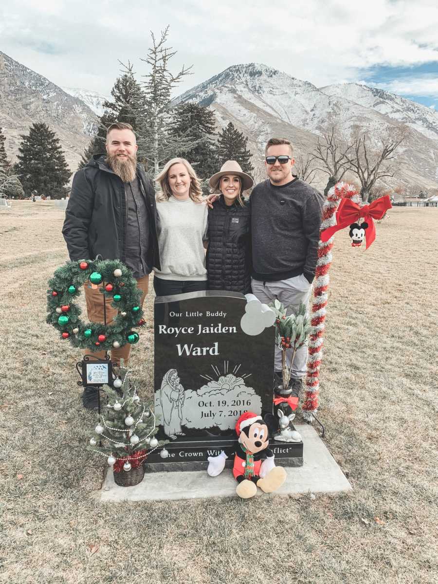 Two married couples stand behind headstone decorated for Christmas for one couples son and other's nephew