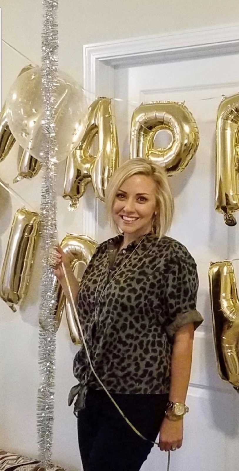 Woman who cut her hair smiles as she holds balloon in front of Happy Birthday sign