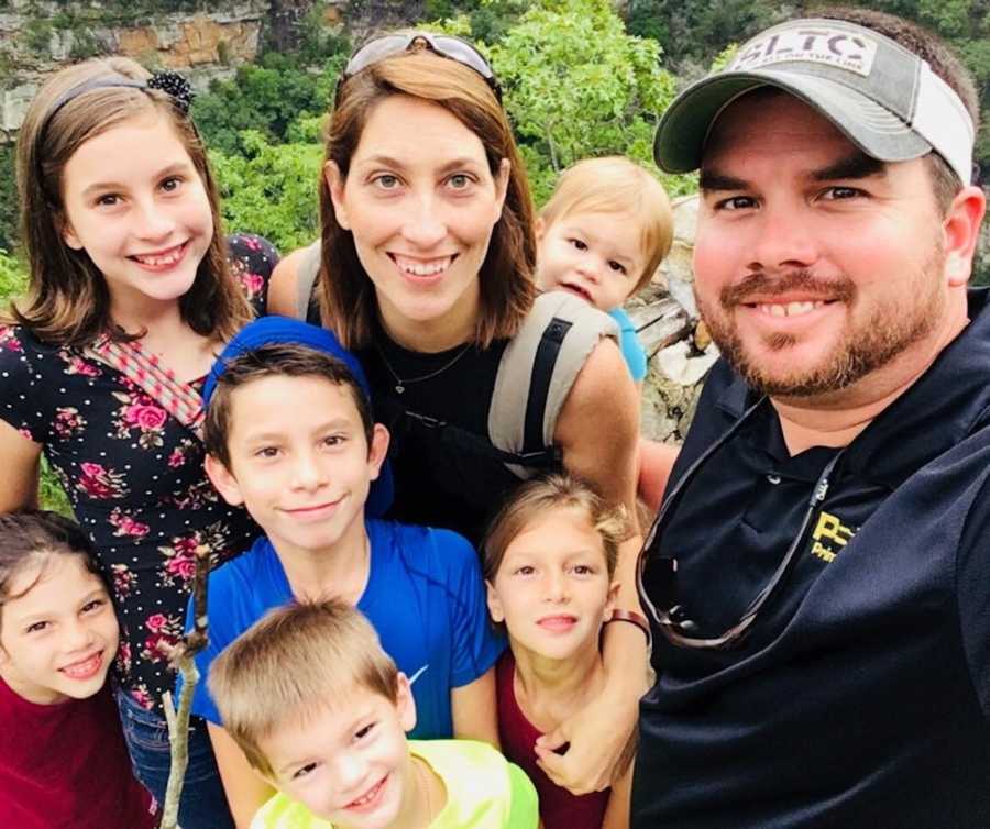 Husband smiles in selfie with wife who holds their youngest beside their five other kids