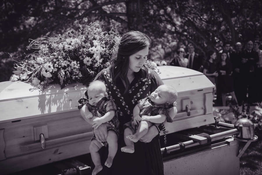 Mother stands besides husband's casket holding her twin baby boys