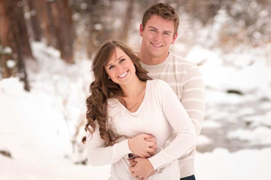 Boyfriend holds girlfriend from behind outside in snowy weather