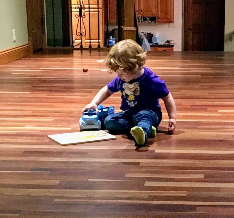 Little boy sits on wooden floor of home playing with toy truck
