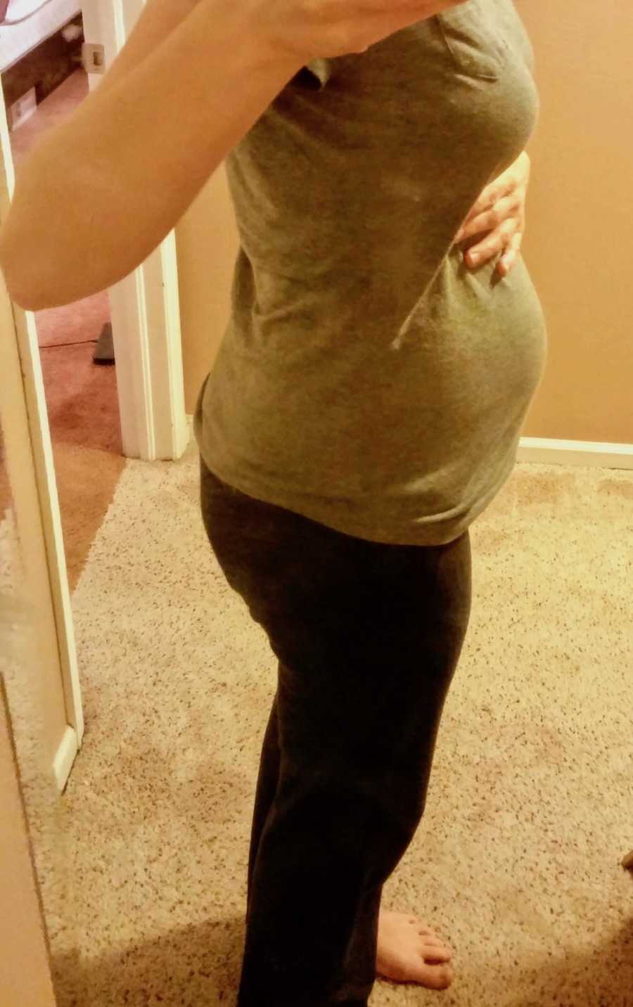 Pregnant woman stands with hand on stomach in mirror selfie