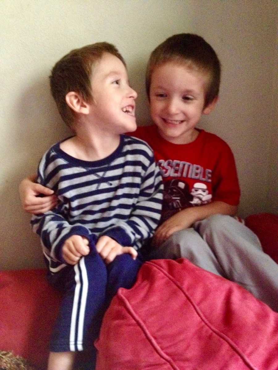 Twin toddlers with cerebral palsy sit on red couch smiling 
