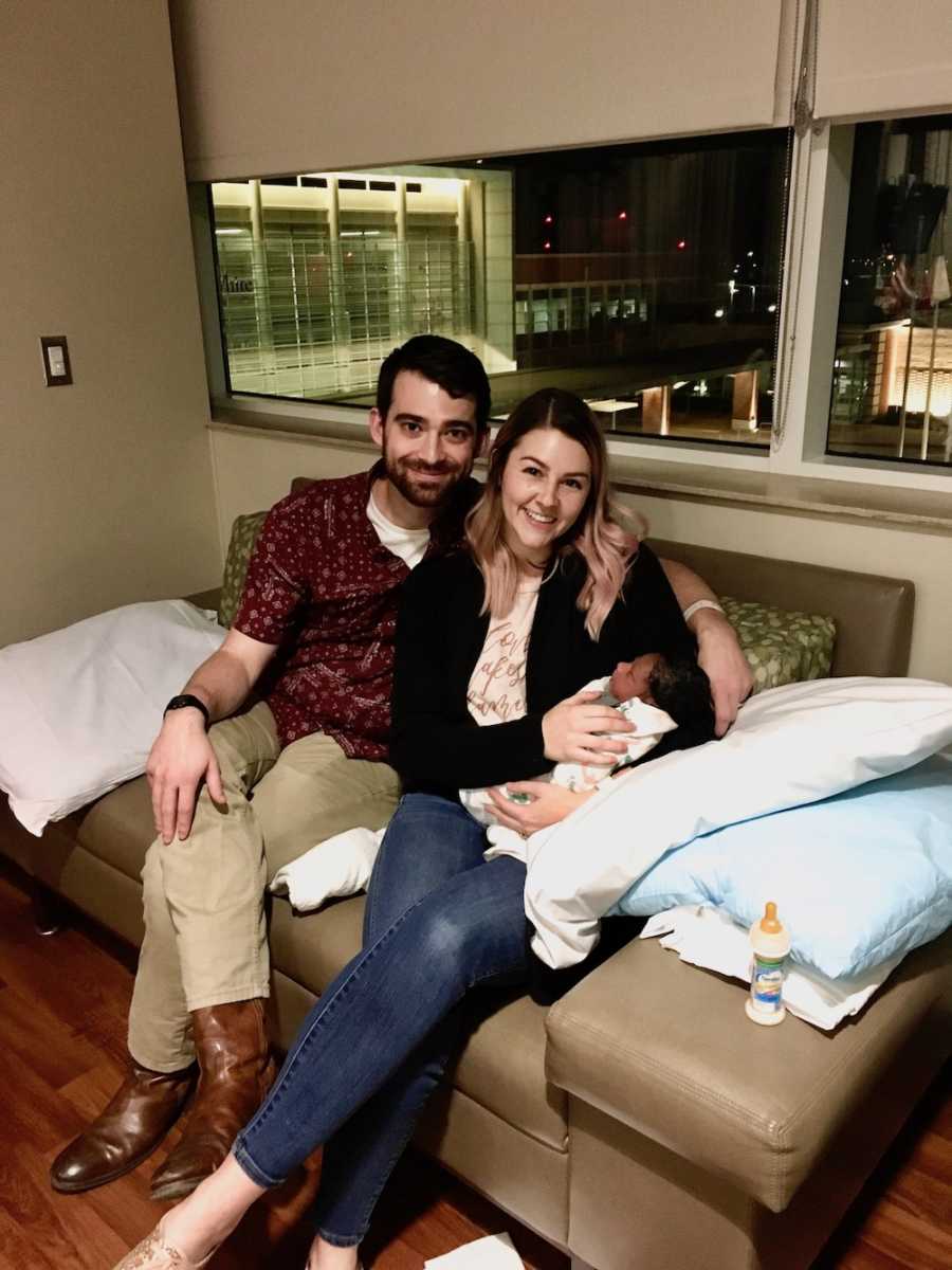 Husband and wife sit on couch holding their adopted newborn