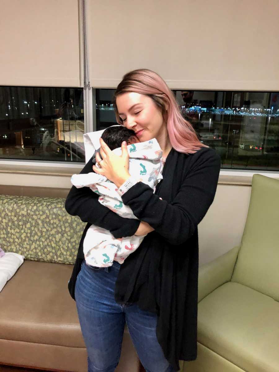 Woman stands in hospital room holding adopted newborn