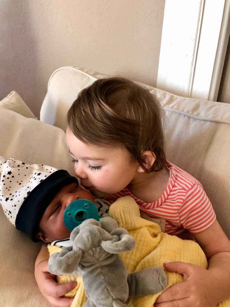 Little girl sits on couch with newborn adopted brother in her lap