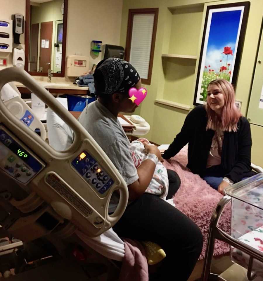 Birth mother sits in hospital bed holding newborn beside woman who is adopting her child