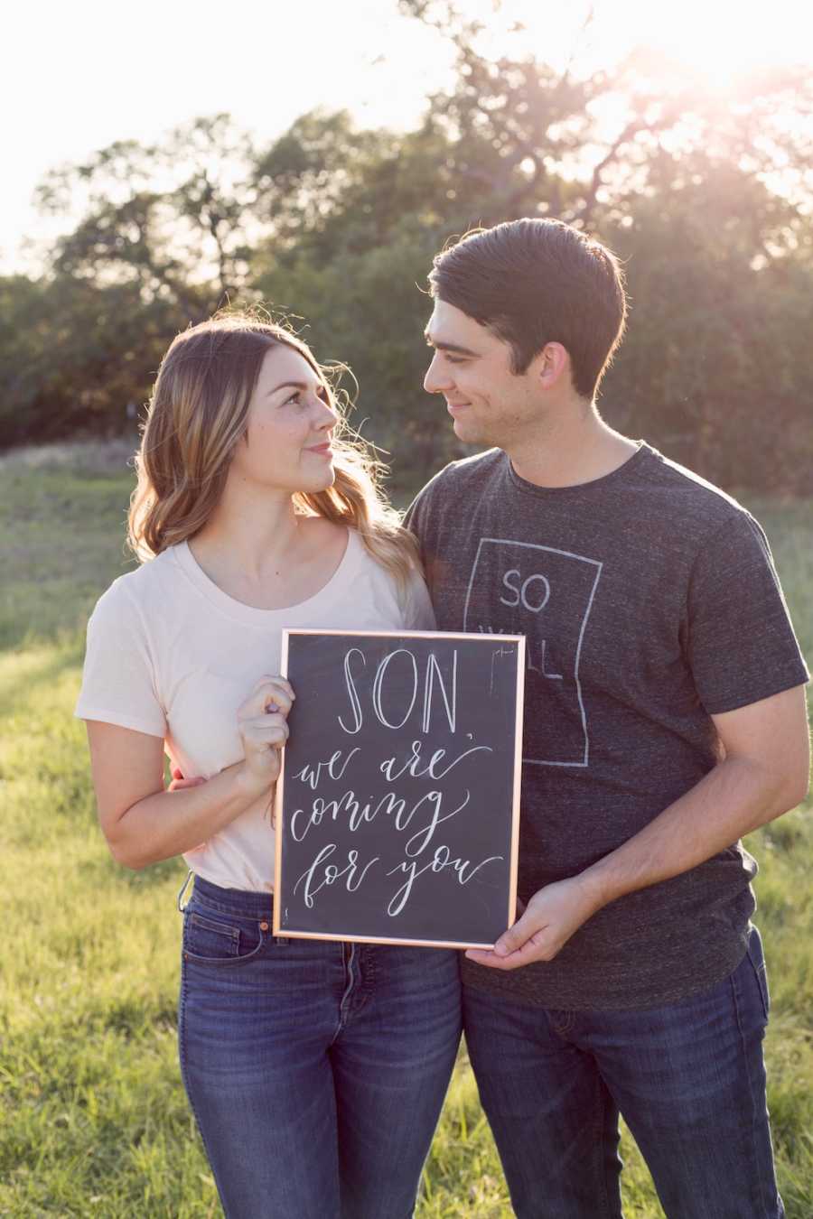 Husband and wife who are going to adopt hold sign saying, "son we are coming for you"