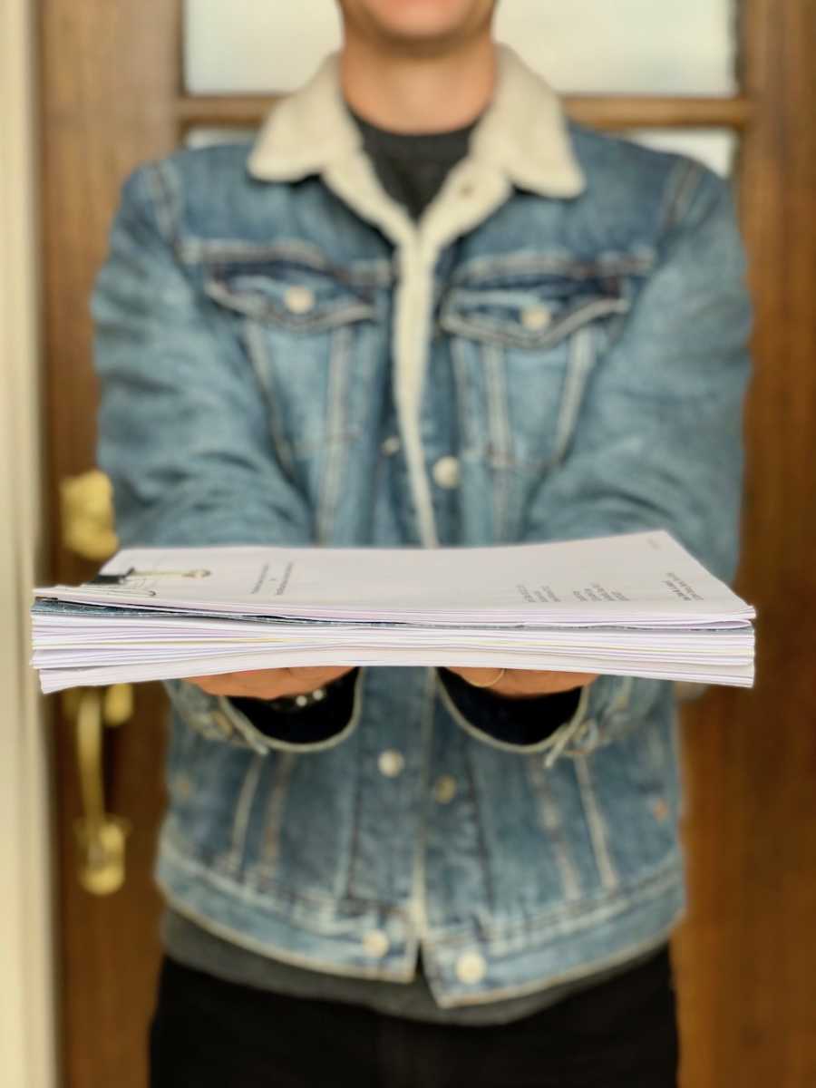 Man stands in front of front door of home holding stack of adoption papers