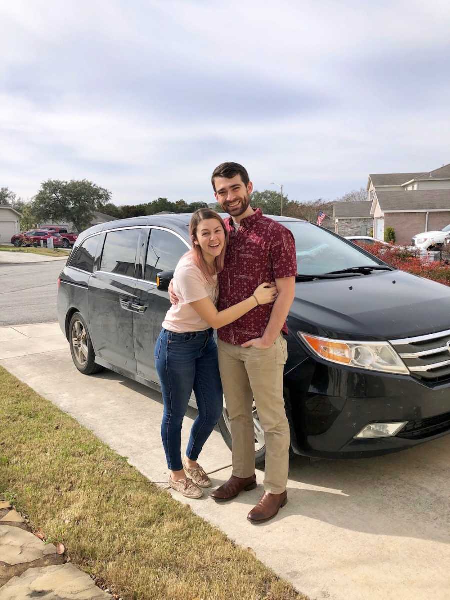 Husband and wife who just got news that they were picked for adoption stand smiling in driveway