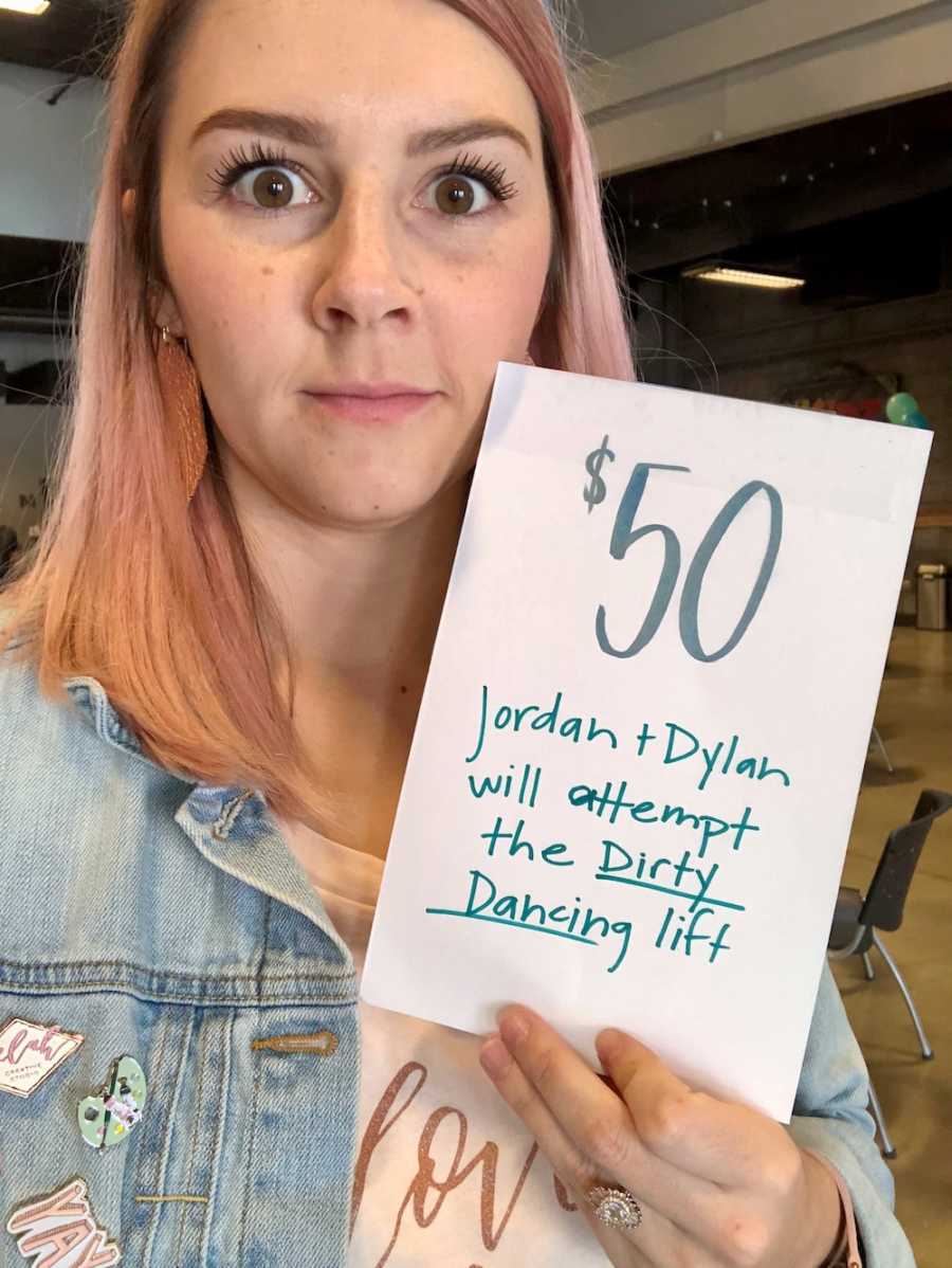 Woman holds up paper in selfie that says, "$50 Jordan + Dylan will attempt the Dirty Dancing lift"