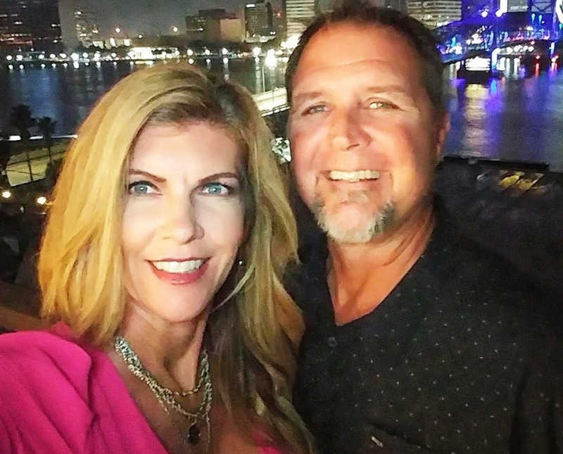 Husband and wife smile in selfie outside at night with city lights in background