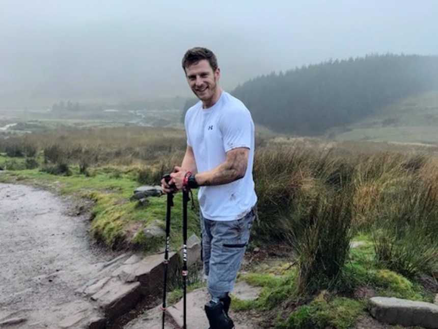Man who was injured in battle stands outside on two prosthetic legs smiling 