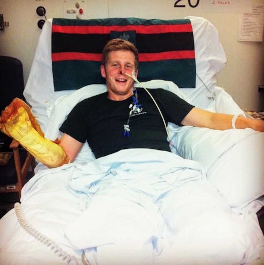 Young man lays in hospital bed smiling after being injured in battle