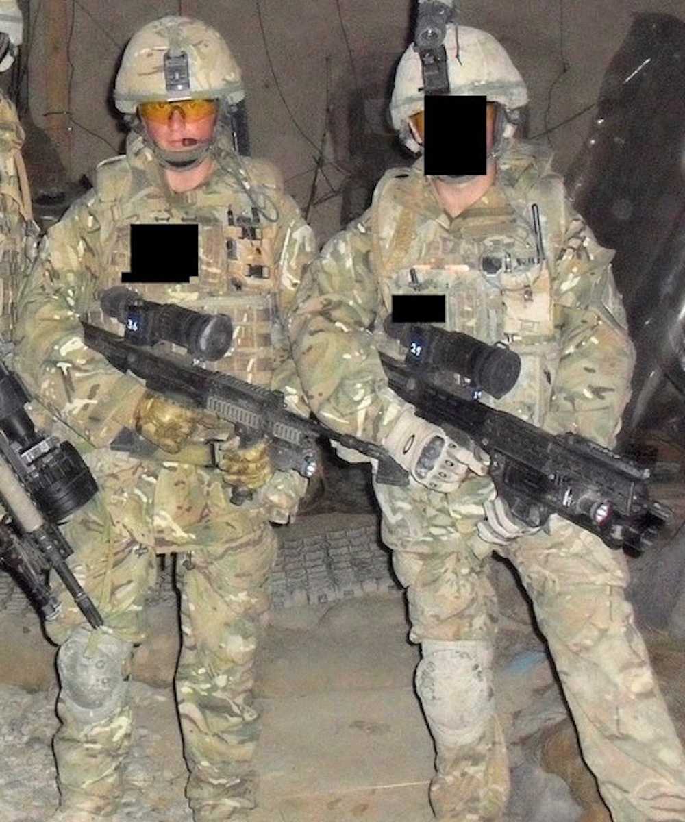 Solder stands holding gun beside another soldier whose face is blocked out