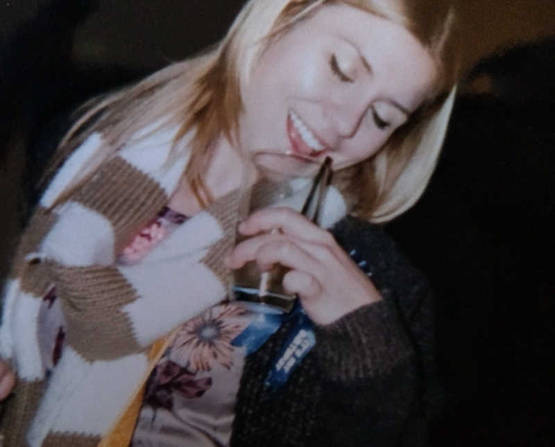 Young woman with alcoholism smiles as she holds drink up to her mouth