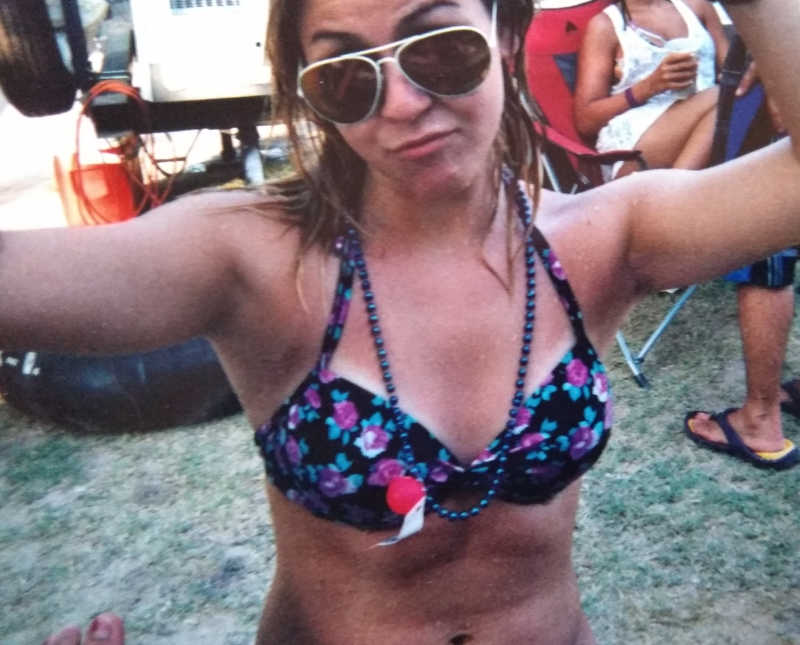 Woman with alcoholism stands outside in bikini top and sunglasses