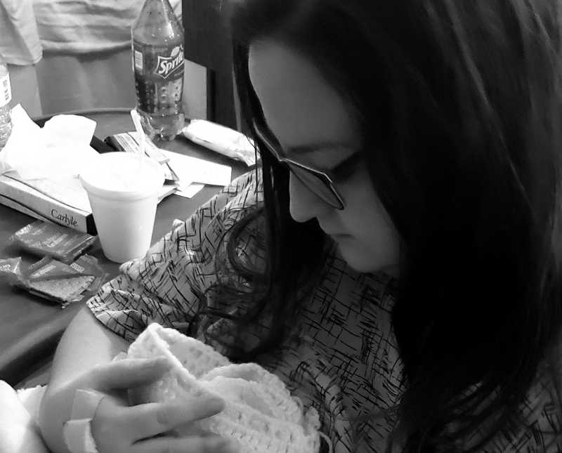 Woman looks down smiling at preemie baby in white blanket in her arms